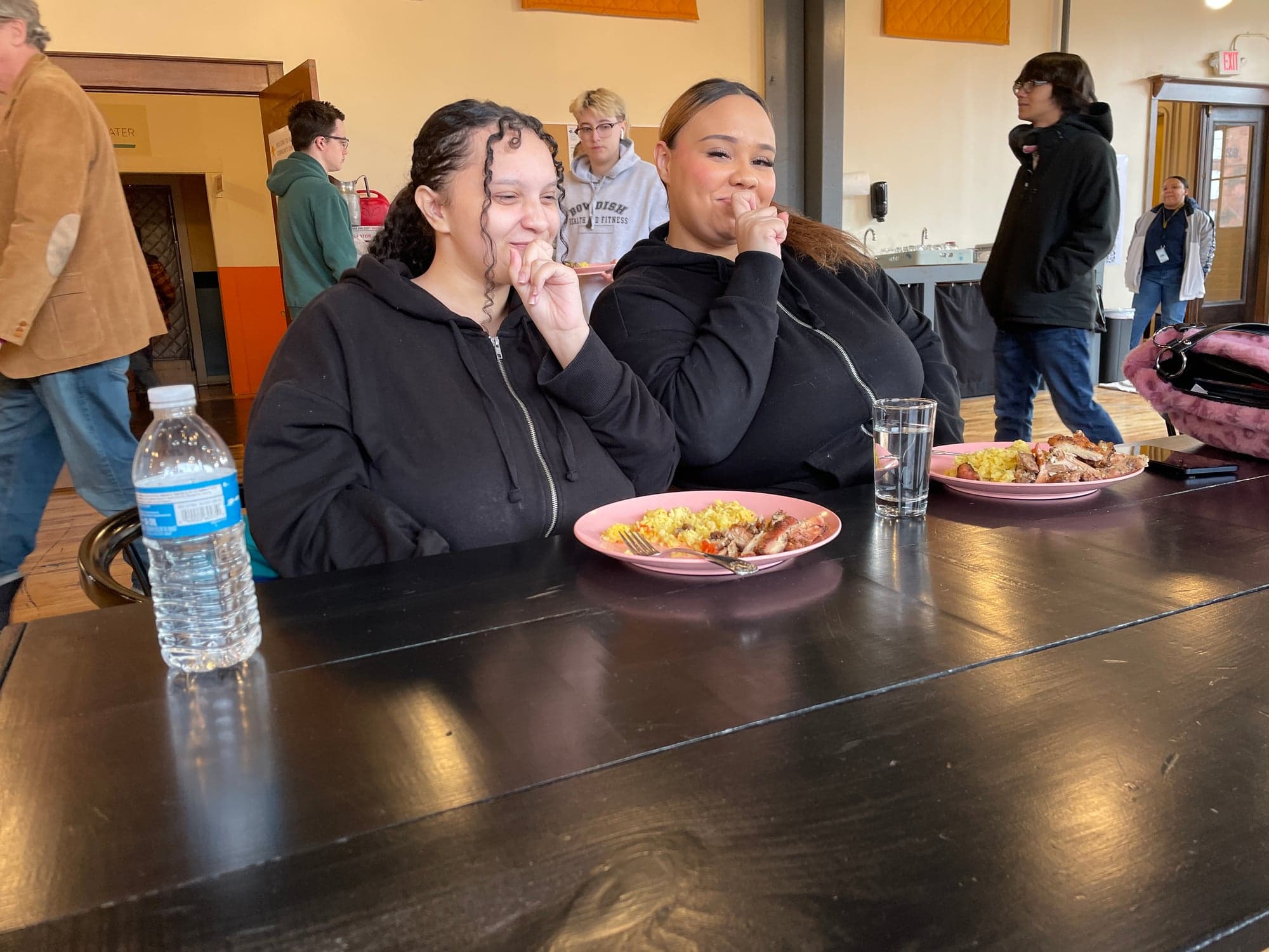 Two students laughing over lunch at the long table