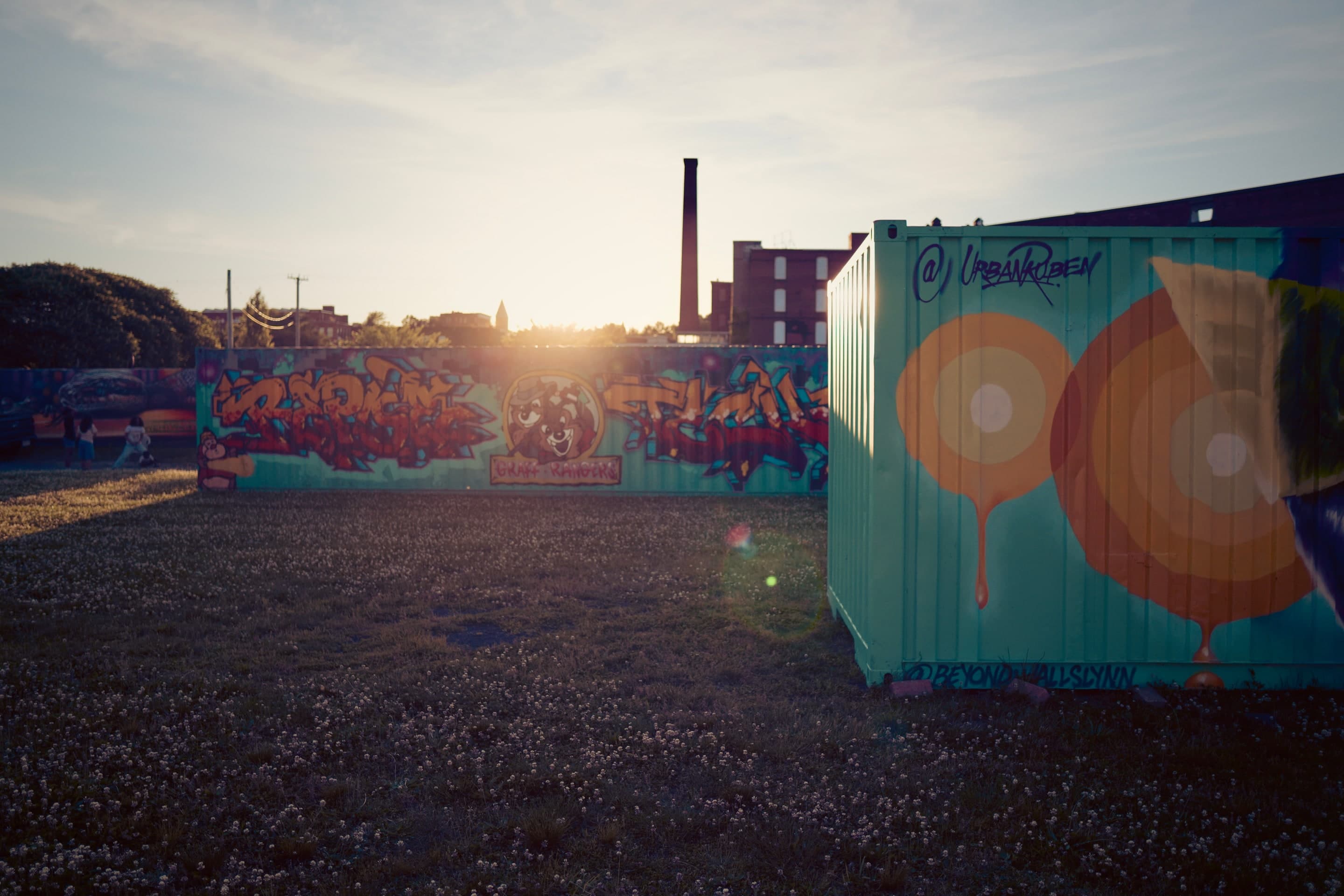 Beyond Walls murals at Armour Yard at golden hour, with a Holyoke mill smokestack behind
